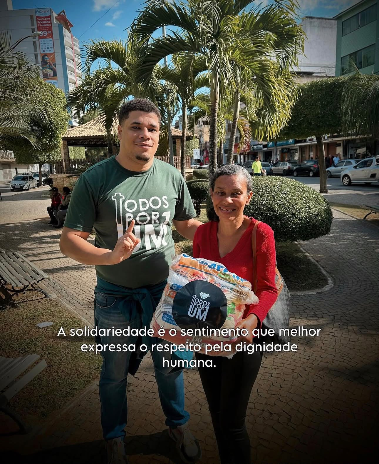 Voluntário da Todos Por Um entregando cesta básica a uma senhora na praça