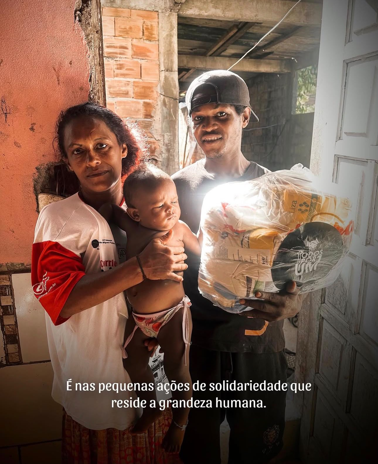 Casal com bebê recebendo uma cesta básica da Todos Por Um na porta de casa